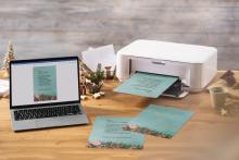 Laptop and printer on table, print Christmas card