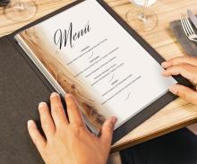 Speisekarte in dunklem Einband, Hände halten sie