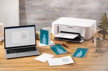 Laptop and printer on desk with greeting cards and fir branches