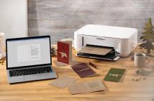 Laptop and printer on wooden table, letter cards and coffee cup