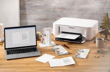 Laptop and printer on wooden table, letters and pens next to it