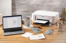 Laptop and printer on wooden desk surrounded by Christmas cards and a cup