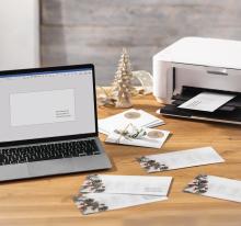Laptop and printer on wooden table, envelopes next to it