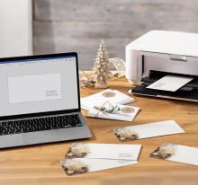 Laptop and printer on wooden table, envelopes in between