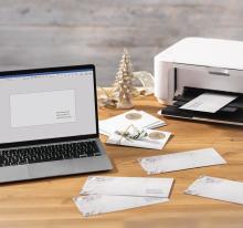 Laptop and printer on wooden table, envelopes in between