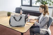 Person tippt an Laptop, Tasche und Pflanze auf Tisch