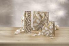 Three gift bags with a pine cone motif stand on a table, a nutcracker can be seen on the left