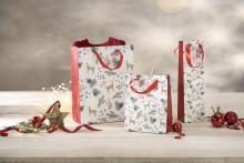 Gift bags with reindeer, fir branches and red ornaments on white table