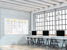 Modern office environment with large windows, row of desks and whiteboard with notes