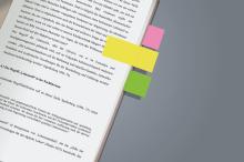 Book page with text and three coloured sticky notes in pink, yellow, green