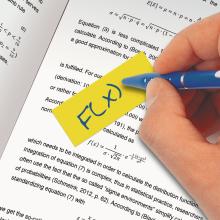 Yellow note with F(x) on book page hand holding blue pen