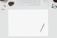 Desk with keyboard, cup, glasses, sheets, pen and blank paper