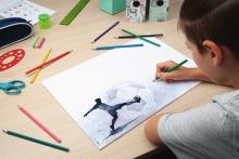 Child draws a footballer desk with pens and school supplies