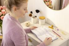 Person schreibt in Notizbuch an Schminktisch