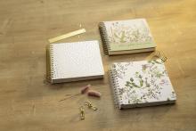 Notizbücher mit floralen Mustern auf Holztisch Goldene Büroklammern daneben