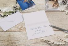 Christmas card with handwritten message "Merry Christmas and Happy New Year!" on a wooden table, surrounded by envelope and decorations
