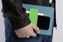Person hält ein blaues Notizbuch mit grünem Band, Smartphone und Stift