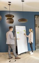 People interacting on a whiteboard in an office ceiling lamps and blue wall in the background