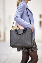 Person mit hellblauem Mantel trägt graue Tasche, Inhalt sichtbar