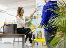 Person pinnt Notiz an Wand, daneben eine Person in blauem Hoodie