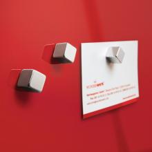 Silberne Magnete auf rotem Hintergrund, ein Magnet hält ein weißes Papier