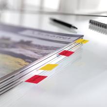 Stack of paper with colorful sticky notes on glass surface, pen and notebook in background