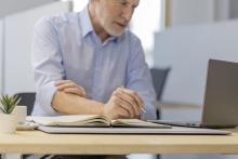 Älterer Mann schreibt in Notizbuch Laptop auf dem Tisch