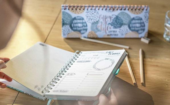 Frau blättert in Kalender, dahinter steht ein Tischkalender in Blautönen