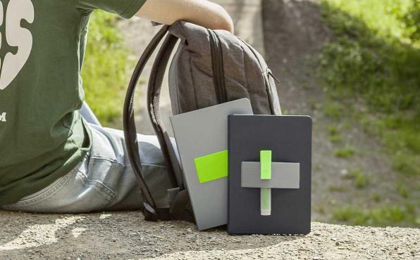 Junger Mann sitzt im Freien, angelehnt an Rucksack mit Linescape Neo Notizbüchern in grau