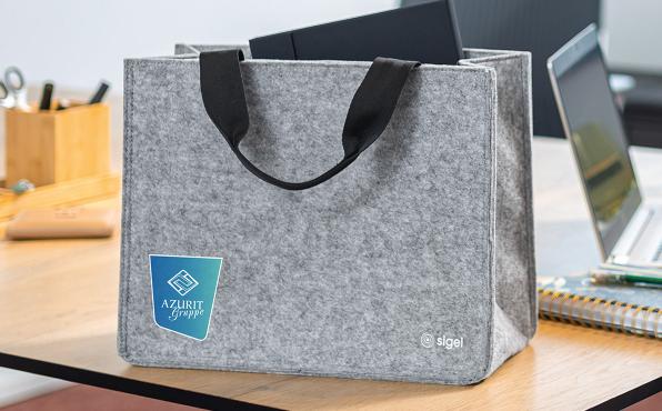Graue Filz Desk Sharing Bag mit Logoaufdruck steht auf einem Schreibtisch