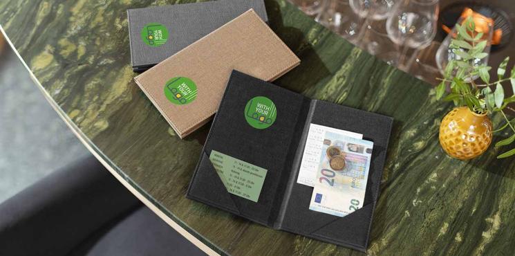 Auf eine Bartheke liegen unterschiedliche Rechnungsmappen mit Logoaufdruck