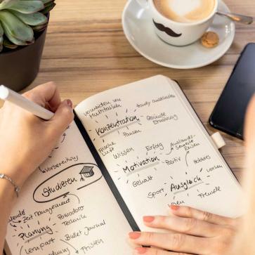 Frau schreibt in Notizbuch Notizen zu Studium