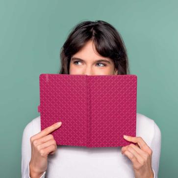 Frau hält Notizbuch in den Händen und schaut dahinter hervor