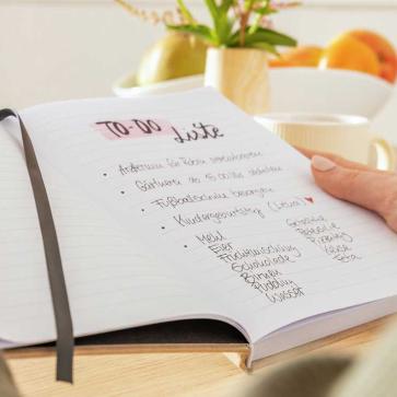 Frau hält Notizbuch mit To-do Liste in den Händen